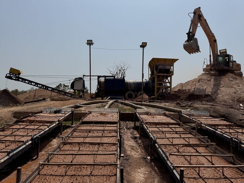 Trommel de lavage en production sur un chantier, alimenté par une pelle, avec ses sluices de récupération au premier plan.